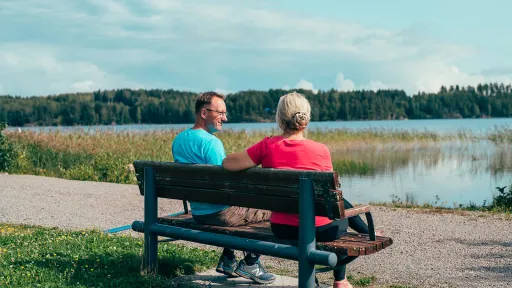 Pariskunta istuu penkillä järven rannalla.