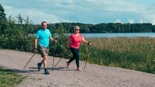 Pariskunta sauvakävelee järven rannalla.