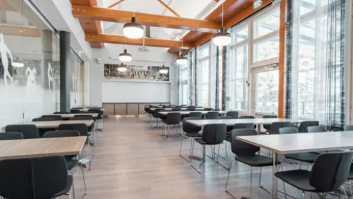 Avara kahvila, vaaleat puupalkit, mustat tuolit, isot ikkunat.