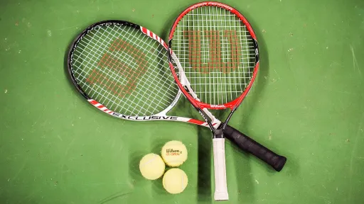 Tennismailat kentällä maassa ristikkäin ja kolme tennispalloa vieressä