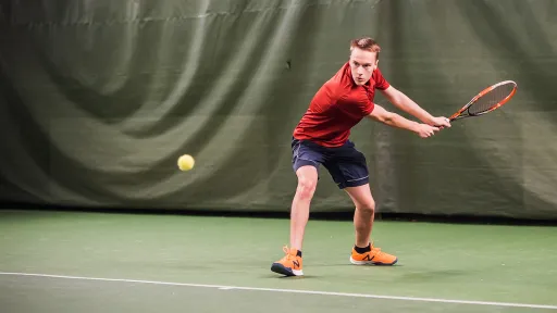 Tennispelaaja lyömässä palloa sisäkentällä.