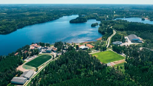 Ilmakuva järvestä ja metsäisestä maisemasta, jossa urheilukenttiä ja rakennuksia.