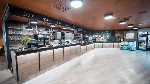 Moderni kahvila, puupaneelein koristeltu tiski ja valaistut hyllyt.