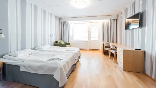 Kaksi sänkyä, vaalea huone, ikkuna, kirjoituspöytä ja tuoli.