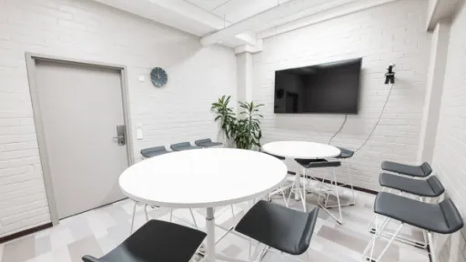 Tyylikäs kokoushuone, kaksi pyöreää pöytää, tuoleja ja seinällä televisio.