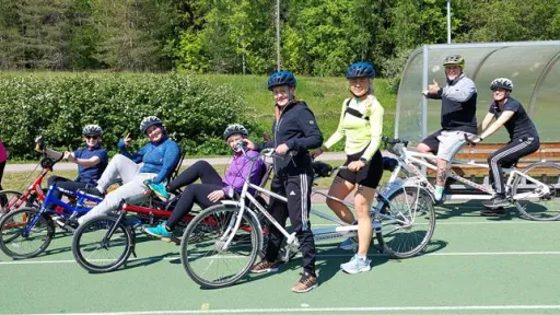 Joukko ihmisiä pyöräilemässä ulkokentällä, kaikki kypärissä.