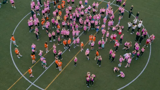 Crowd of people in pink and orange shirts on a sports field.