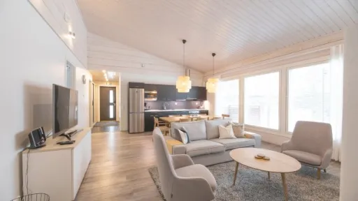 Valoisa olohuone ja keittiö avarassa hirsitalossa, vaaleat kalusteet ja isot ikkunat.