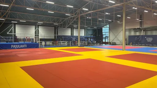 Pajulahden kamppailuareena. Tyhjä judohalli, värikkäät tatamit, teräksiset kattopalkit.