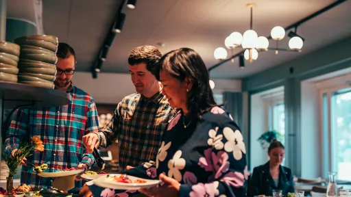 Kolme ihmistä seisoo buffet-pöydän ääressä ravintolassa.