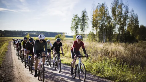 Gravel-pyöräilijät maaseudun soratiellä aurinkoisessa säässä.