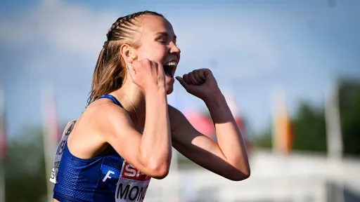 Urheilija juhlii iloisesti kentällä, taustalla näkyy lipputankoja.