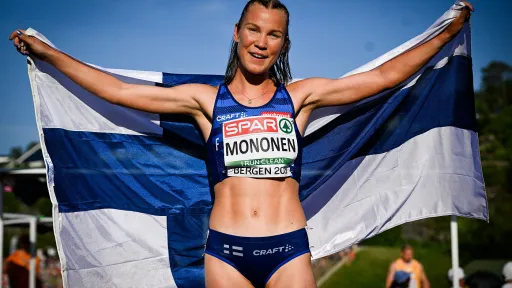 Yleisurheilija hymyilee ja pitää Suomen lippua.