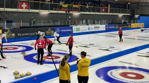 Curling-ottelu hallissa, pelaajat keltaisissa ja punaisissa paidoissa. Yleisö katsomossa.