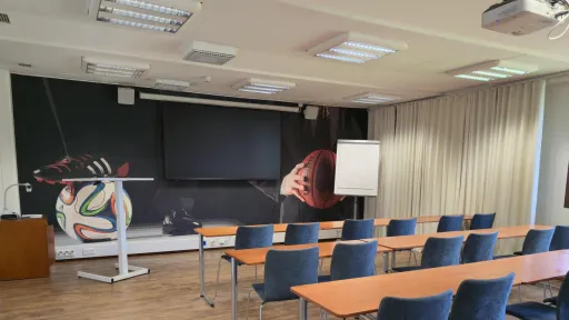 Tyhjä luokkahuone, jossa puiset pöydät ja siniset tuolit.