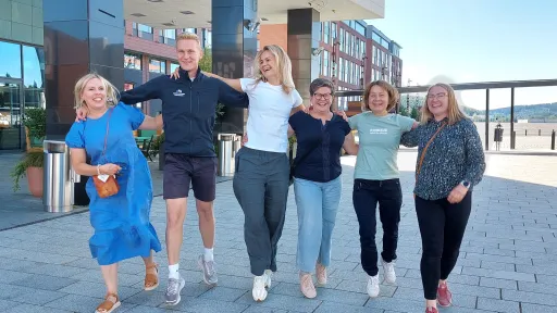 Iloinen ryhmä kuusi ihmistä kävelee yhdessä ulkona.