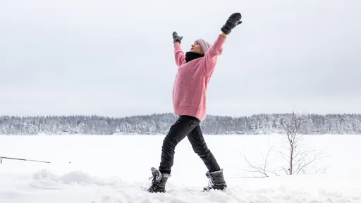 Nainen joogaa iloisesti lumisessa järvimaisemassa.