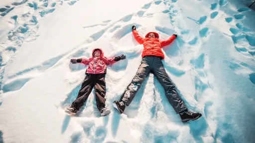 Äiti ja tytär tekevät lumessa lumienkeleitä.