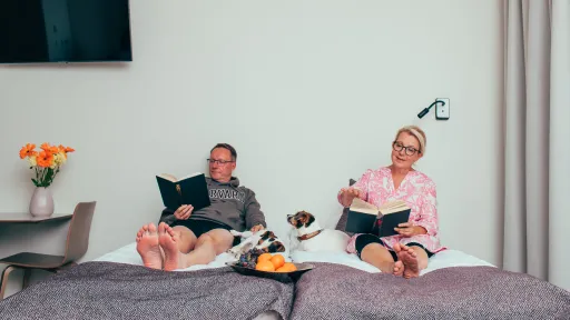 Pariskunta lukee sängyssä kirjojaan Pajulahden hotellissa koiran makoillessa heidän keskellään.