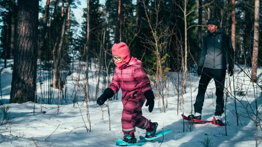 Tyttö ja nainen lumikenkäilevät lumisessa metsässä.