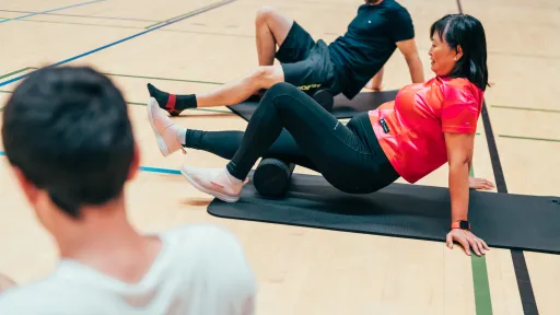 Kaksi ihmistä pyörittelee foam rollereita jalkansa alla.