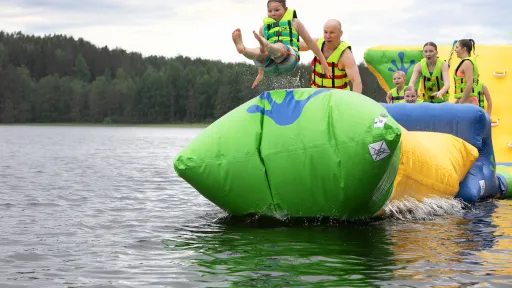 Lapsi hyppää ilmapatjalta järveen muiden katsoessa taustalla.