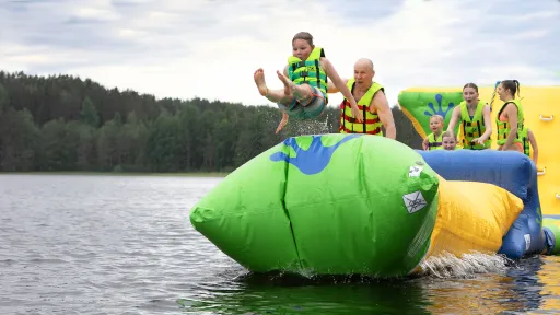 Lapsi hyppää ilmapatjalta järveen muiden katsoessa taustalla.