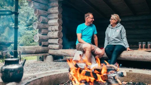 Couple sitting by a campfire in a log cabin, smiling at each other.