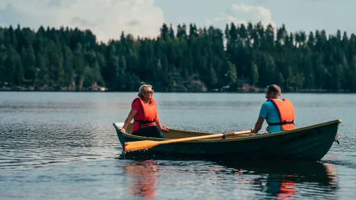 Two people in life vests rowing a boat on a calm lake.