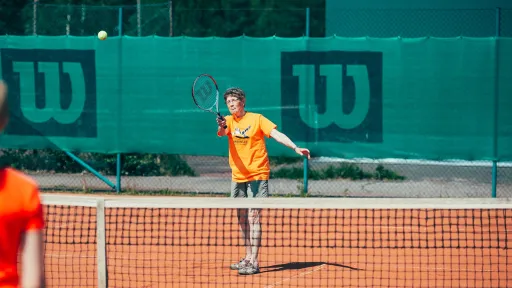 Tennis player in orange shirt serving on clay court.