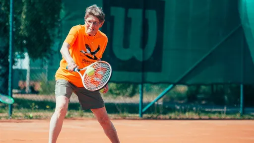 Tennis player in orange shirt on clay court, mid-swing.