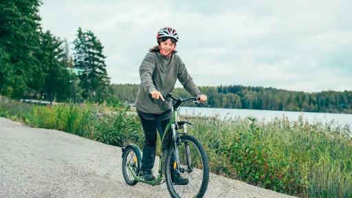 Nainen potkii kickbikella järven rannalla.