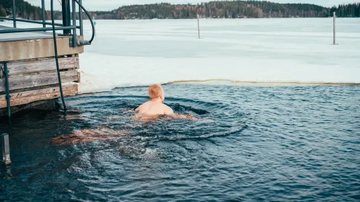 Person swimming in icy lake near a wooden platform.