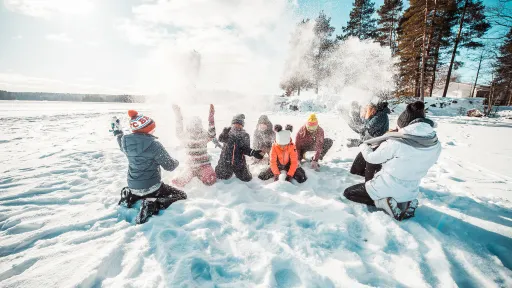 People playing in snow, surrounded by trees under a clear sky.
