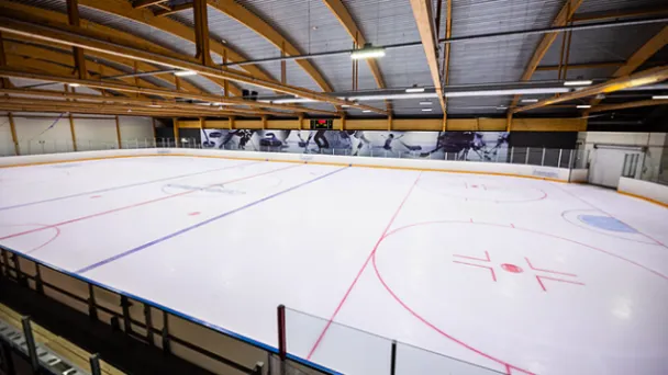 Indoor ice hockey rink with painted lines and wooden ceiling.