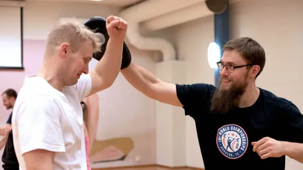 Mies nostaa toisen miehen kättä kehässä, iloinen tunnelma.