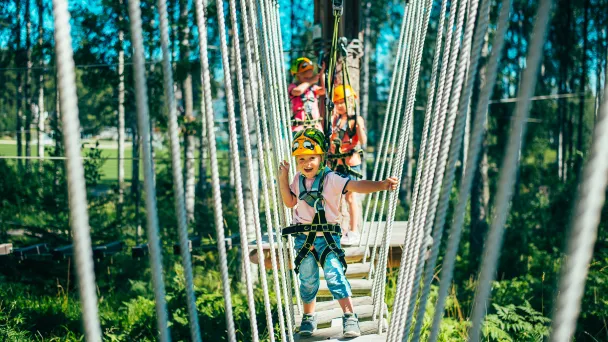 Kaksi lasta seikkailee köysiradalla metsässä.