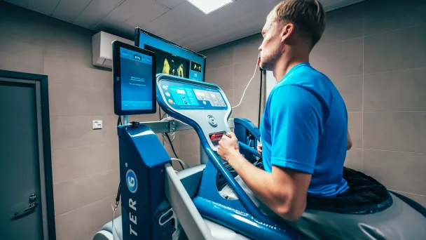 Mies juoksee kuntolaitteella kuntosalilla tarkkaillen näyttöä.