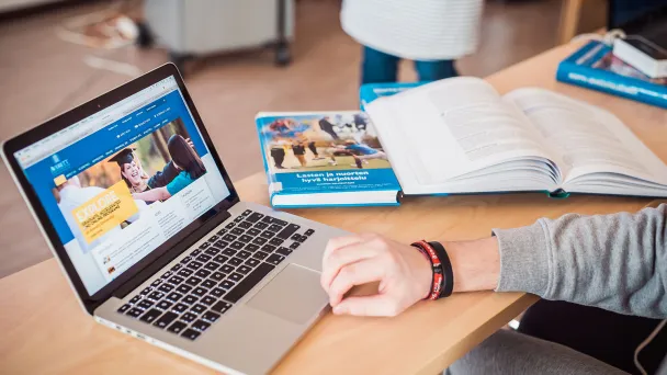 Laptop and open book on a desk, person working.