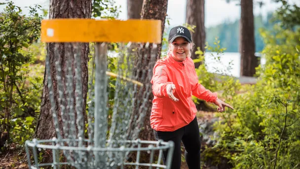 Person playing disc golf, about to throw a disc toward the target in a forest setting.