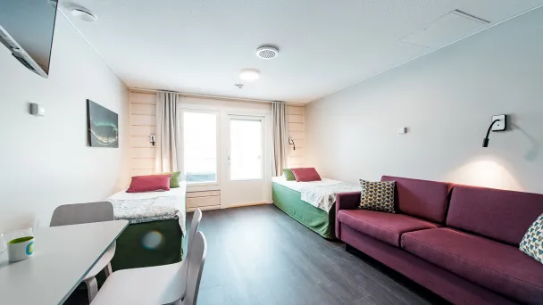 Valoisa hotelli­huone kahdella sängyllä, sohvalla ja parveke­näkymällä.