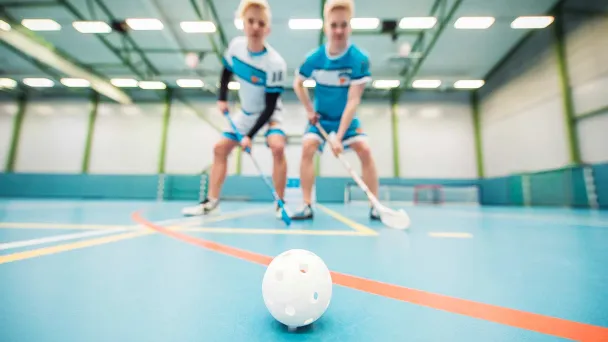 Kaksi salibandypelaajaa tavoittelee palloa sisätiloissa.