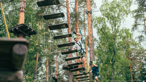 Seikkailupuistossa ihminen kävelee köysisillalla metsän keskellä.