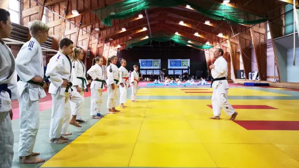 Judo-opettaja ohjaa opiskelijoita tatamilla sisätiloissa.