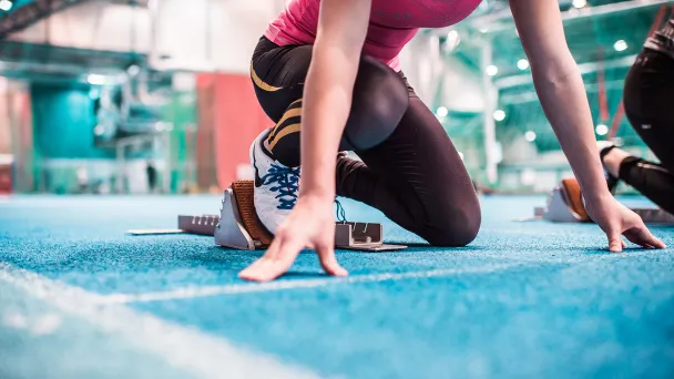 Athletes in starting position on blue indoor track.