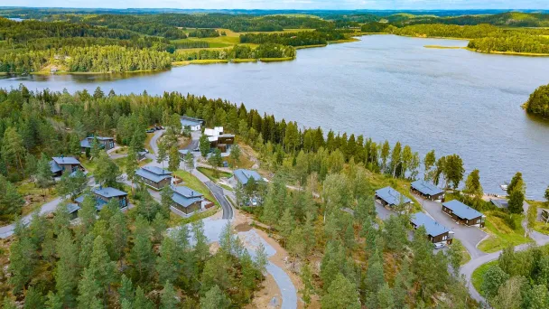 Ilmakuva metsän ympäröimästä järvimaisemasta ja mökeistä.