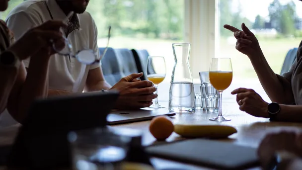 Ikkunan äärellä istuvia ihmisiä, pöydällä mehua ja hedelmiä.