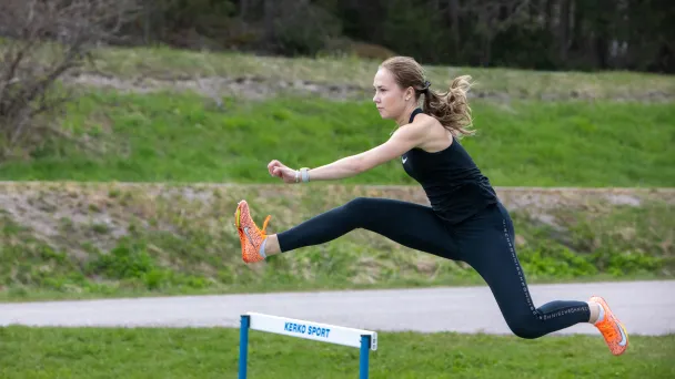 Athlete in mid-air, jumping over a hurdle outdoors.