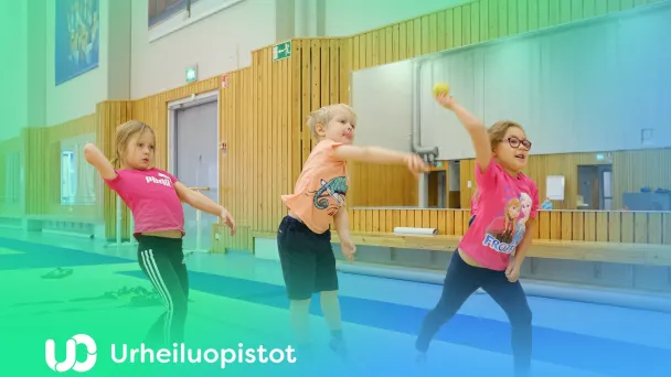 Kolme lasta heittelee palloja sisätiloissa, iloisen värikäs ympäristö.