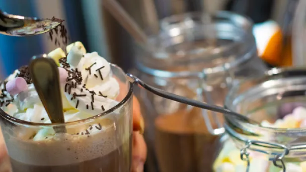 Kermavaahto koristeltu kuuma kaakao, käsi lusikoi koristeita.